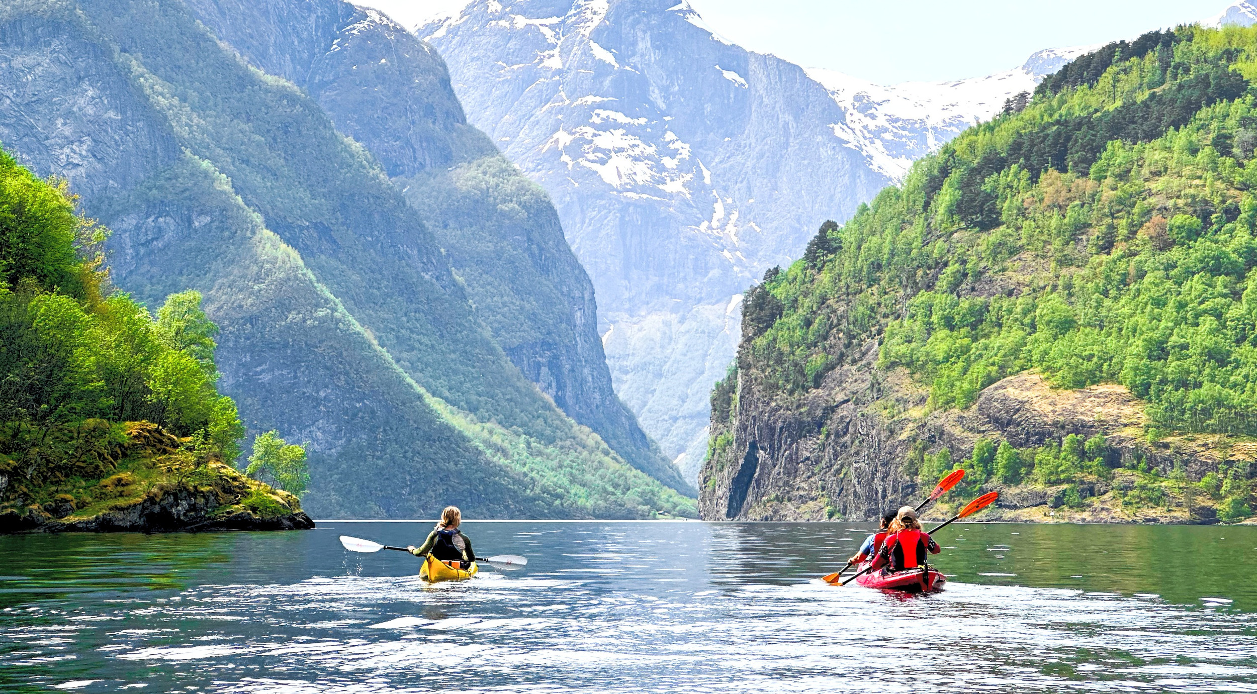 Kayaks navigating a deep blue Norwegian fjord surrounded by cliffs