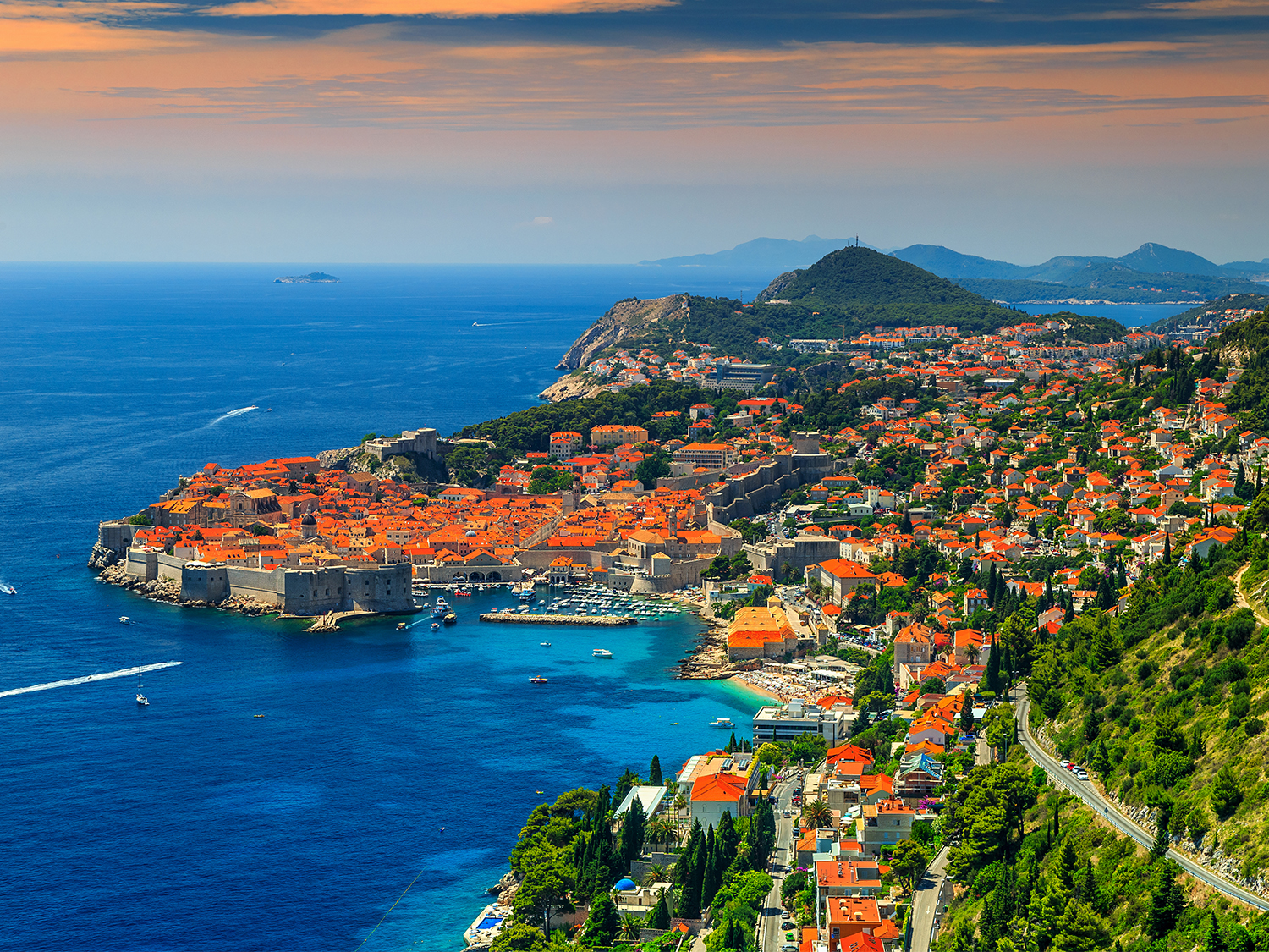 A sailboat on clear turquoise waters near a historic European coastline